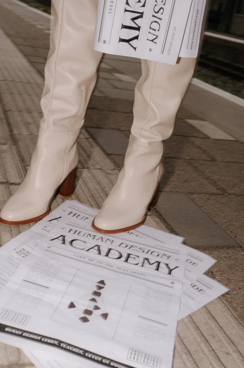 Crèmekleurige laarzen tussen exemplaren van de Human Design Academy-krant op de grond