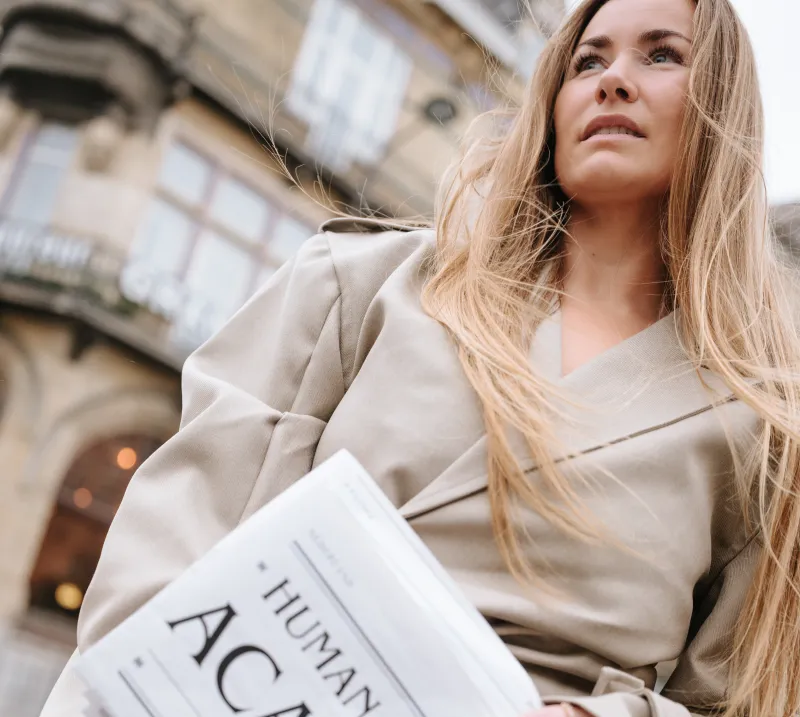 Clenda Moen in een beige trenchcoat met de Human Design Academy-krant onder haar arm